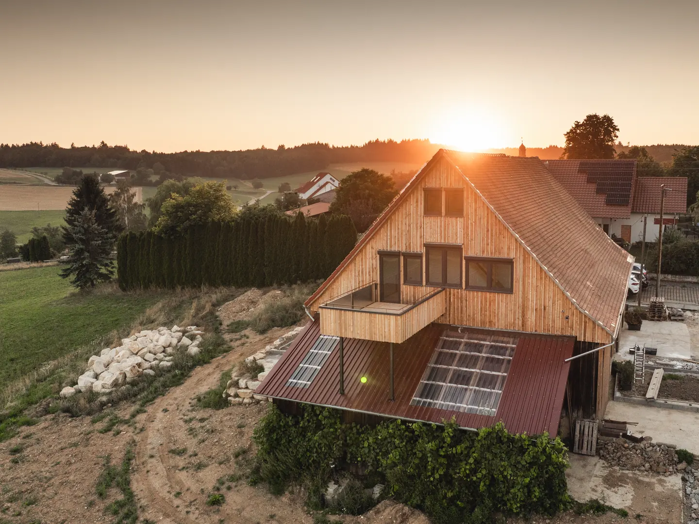 Holzhaus mit Fenstern im Giebel und kleinem Balkon, Luftaufnahme bei Sonnenuntergang.