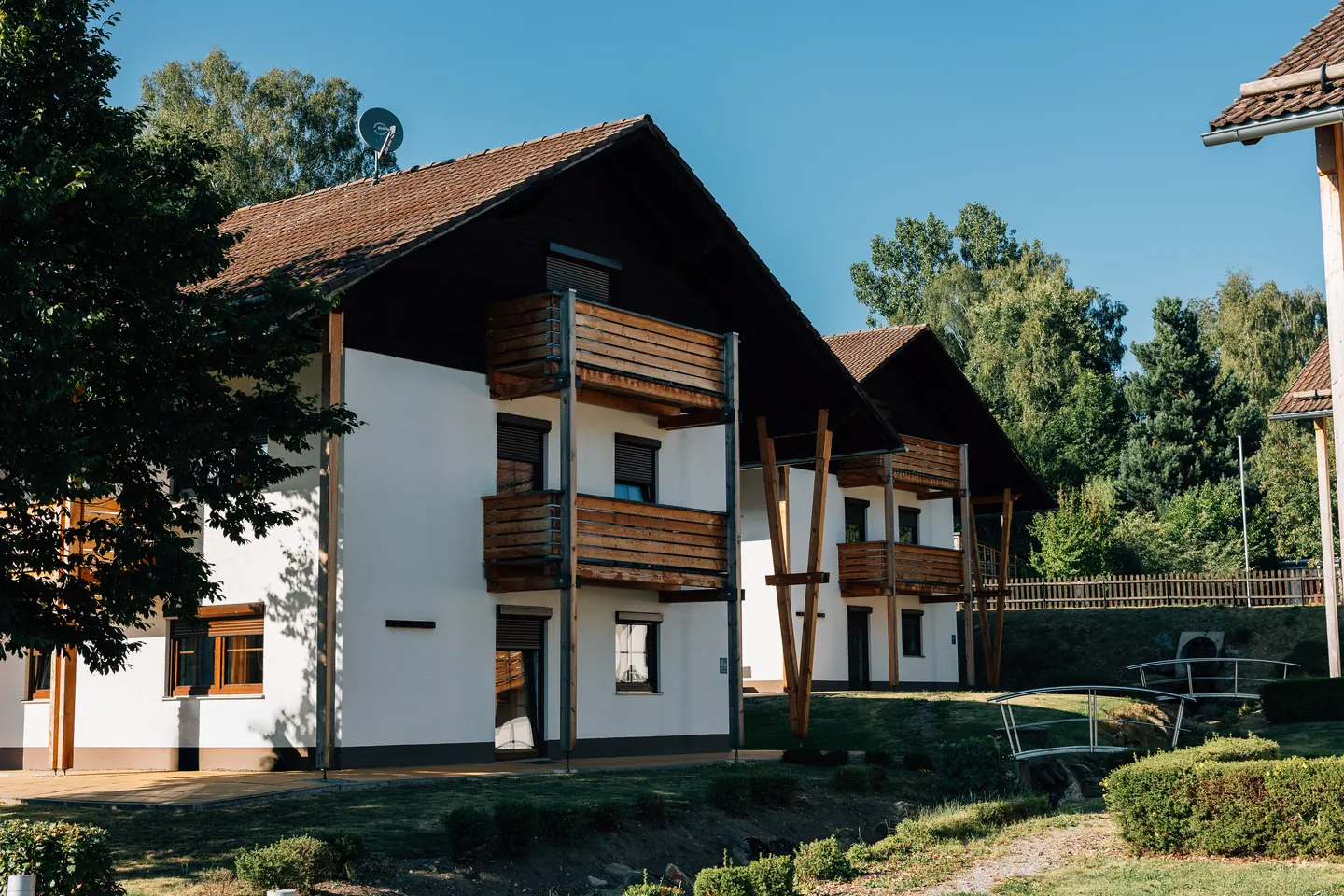 Wohnhäuser mit weißen Fassaden, dunklen Giebeln und Holzbalkonen in einer Gartenanlage.